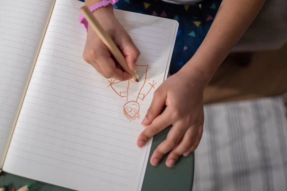manos de un niño, dibujando a una persona en una hoja de papel