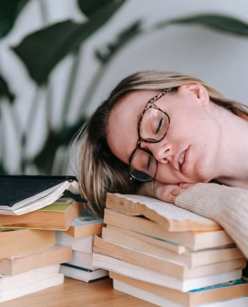 mujer recostada su cabeza sobre unos libros, muy muy cansada, está dormida.