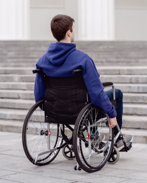 persona usuaria de silla de ruedas frente a una escalera, sin poderla subir